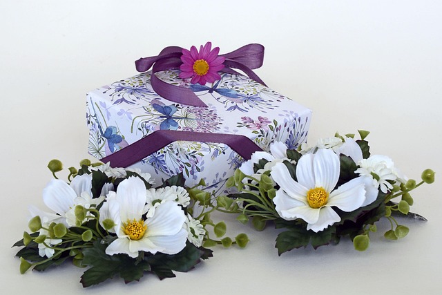 Close-up of hands carefully wrapping a gift box with cream tissue paper, sage green ribbon and dried eucalyptus sprig on a wooden worktable